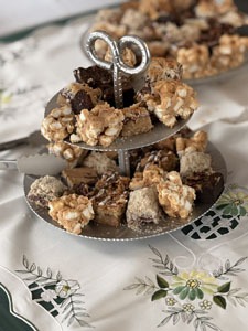 A tiered serving stand holds an assortment of dessert squares on a floral tablecloth.
