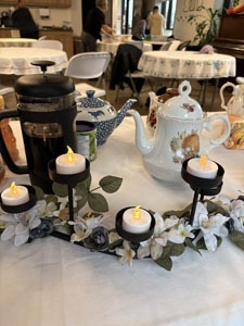 Table decorated with teapots, a French press, and a floral candle arrangement with small glowing tea lights.
