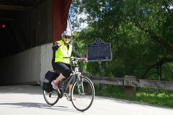 Cyclist wearing a bright yellow safety vest rides a bicycle across the West Montrose covered bridge during the Out-Spok’n Bike-a-Thon.