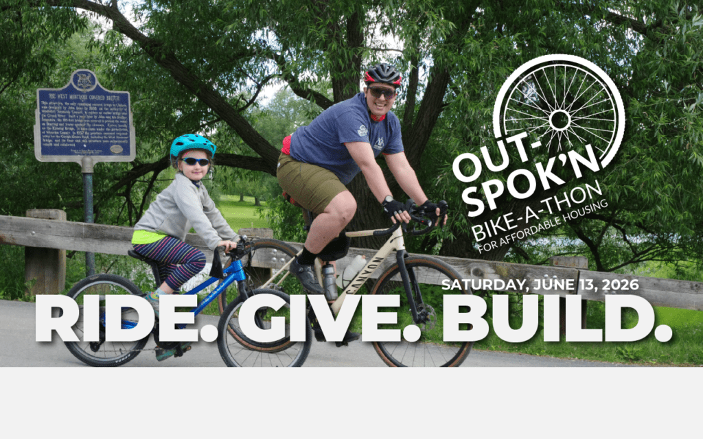 An adult and a child ride bicycles together along a tree-lined path, both wearing helmets and smiling. Overlaid text promotes the “Out Spok’n Bike-a-thon for Affordable Housing” on Saturday, June 13, 2026, with the slogan “Ride. Give. Build.”