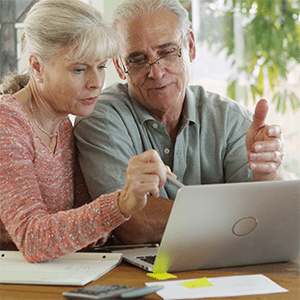 Older couple reviewing information together on a laptop at a table with papers and notes.