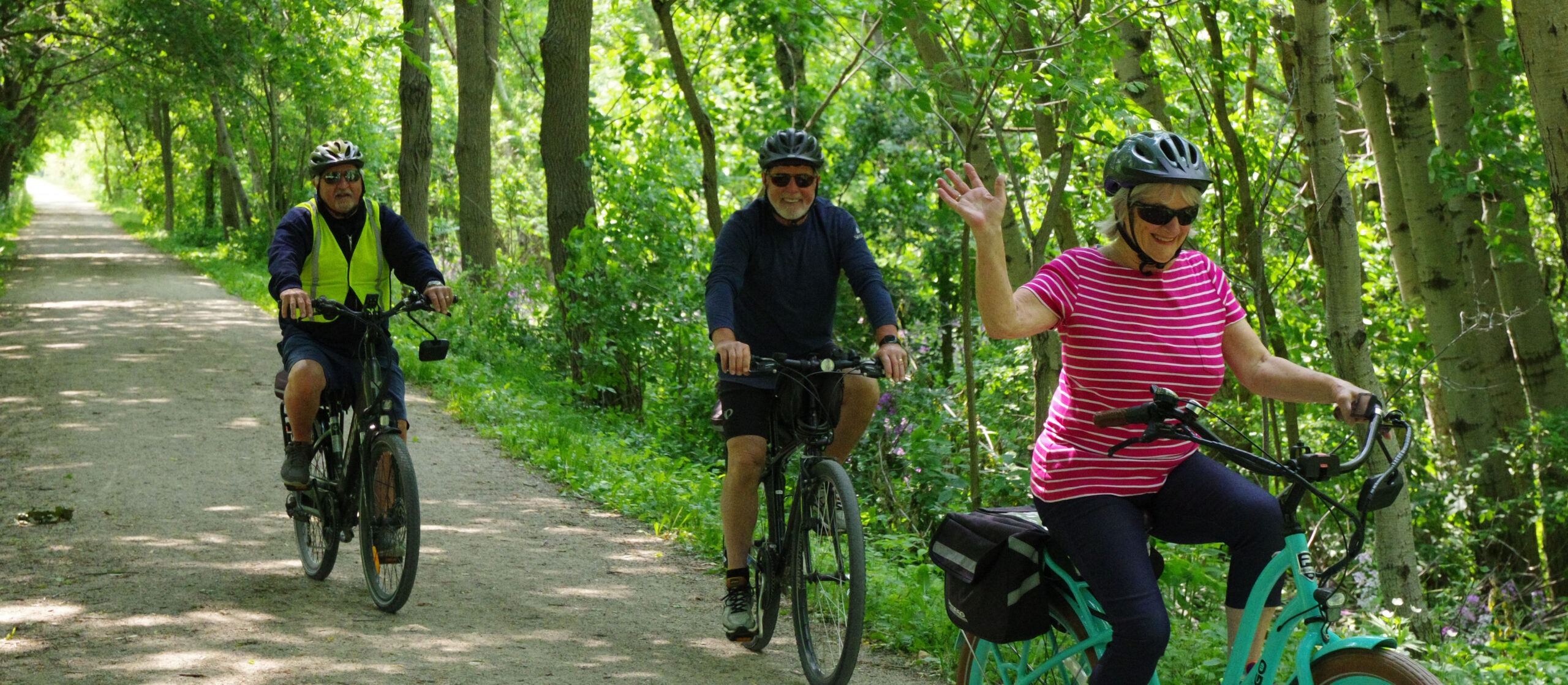 Two men and a woman ride on a path in the woods.