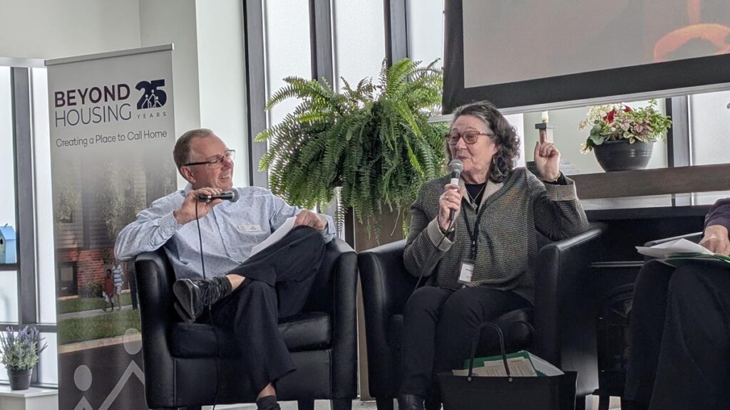Margaret Nally speaks into a microphone during a panel discussion while Dan Driedger listens.