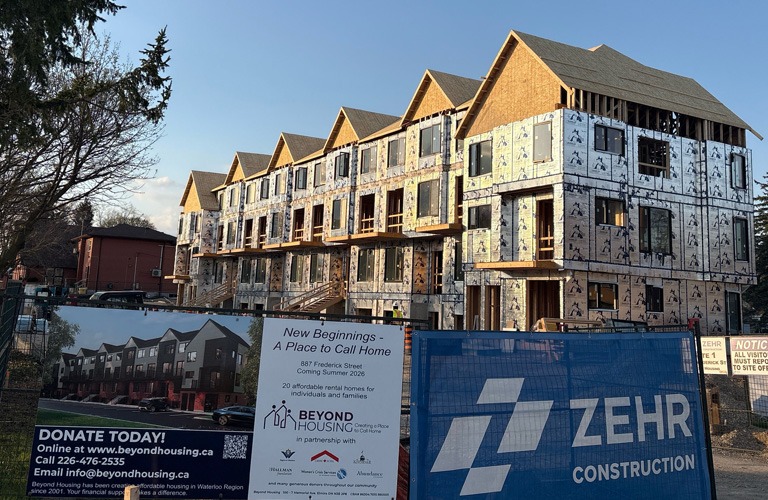 Multi-unit townhome development under construction with project signage and fencing at the front of the site.