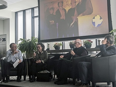 Four panelists seated on a stage participating in a discussion, each holding a microphone during a formal event.