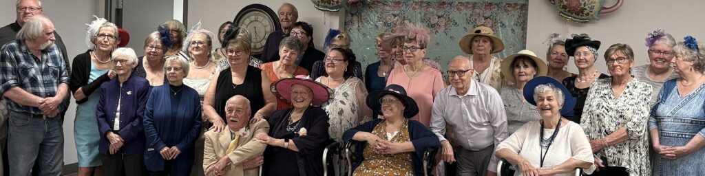 Large group of residents and guests wearing decorative hats and posing together.