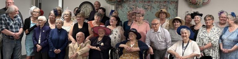 Large group of residents and guests wearing decorative hats and posing together.