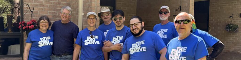 Volunteers wearing matching “The Big Serve” shirts stand together outside Sprucelawn Apartments for Seniors after completing a community service project.