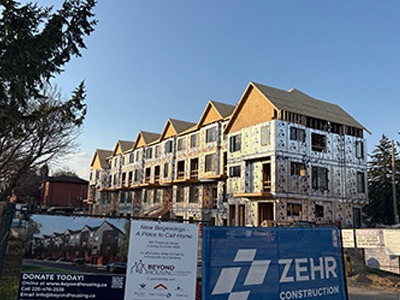 Row of townhomes under construction behind fencing with signage promoting a housing project and construction company.