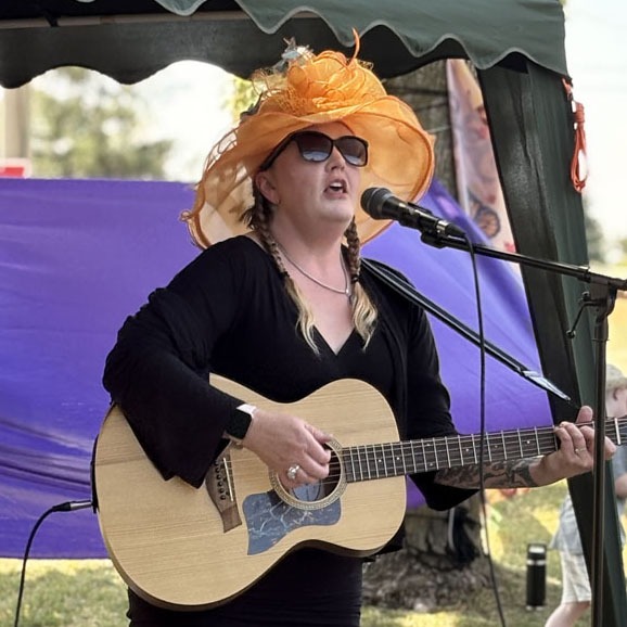 Tenant Dottie Joyce performs with an acoustic guitar on an outdoor stage during the Butterfly Garden celebration.