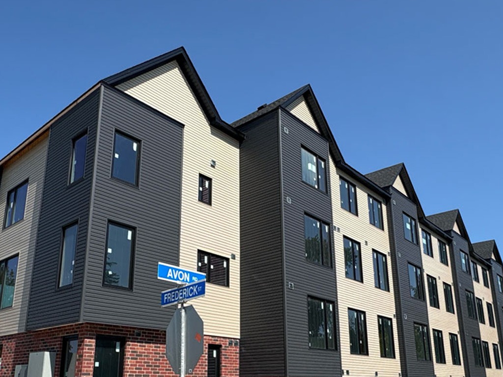 Exterior of the new Beyond Housing townhomes at 887 Frederick Street, with cream and dark grey siding and the Avon and Frederick street signs visible.